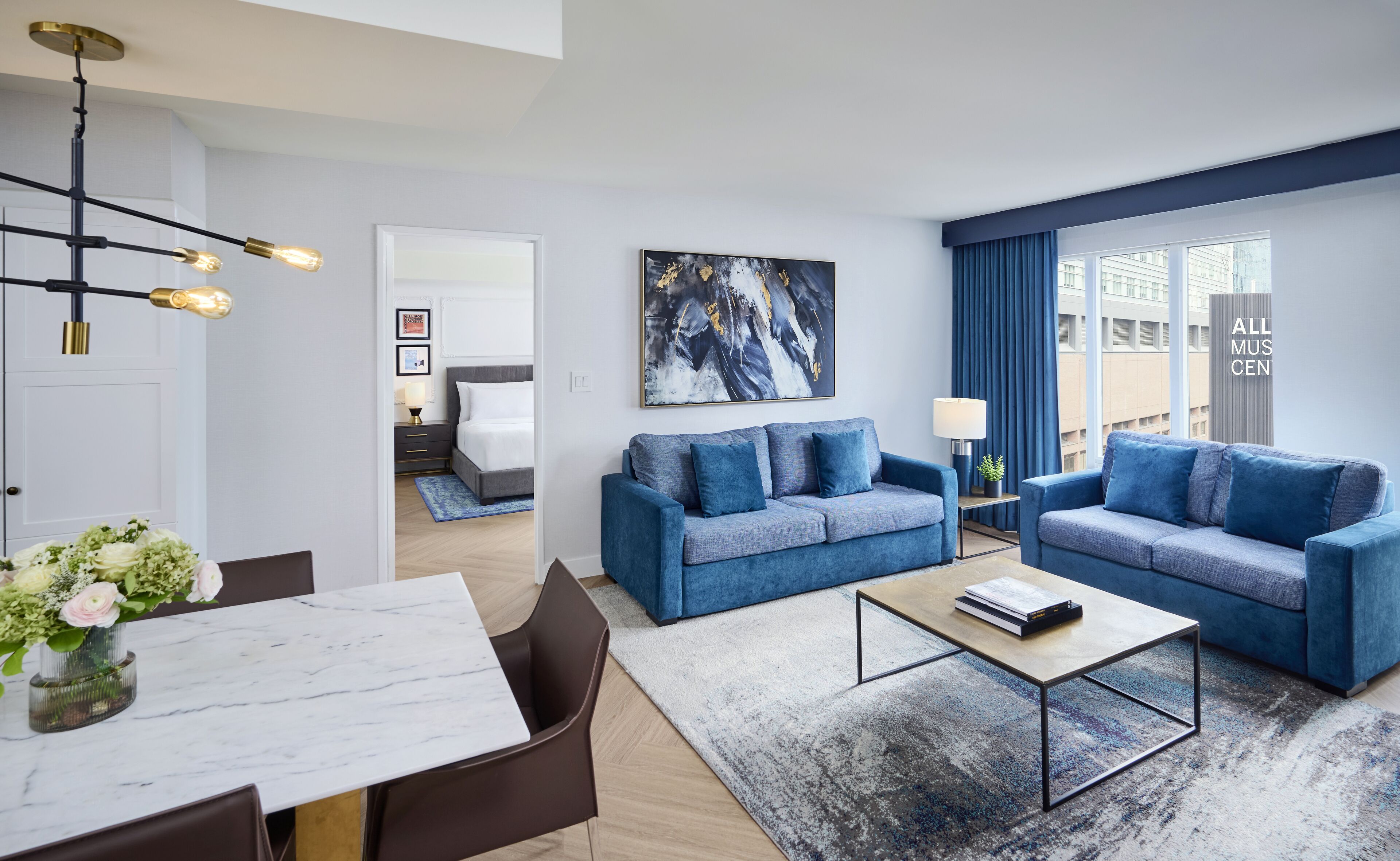 A modern living room with a blue sofa set, a coffee table, and a dining area with a marble table.