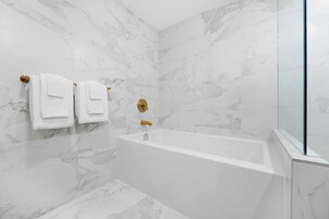 Een moderne badkamer met een vrijstaand bad, marmeren wanden en een douchecabine van glas.