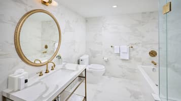 Een moderne badkamer met marmeren wanden, een spiegel met gouden lijst, een witte wastafel, een toilet en een douchecabine met glazen wanden.