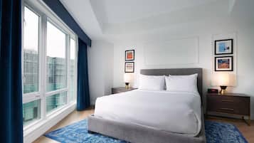 Una habitación de hotel moderna con una cama grande, dos mesitas de noche y un amplio ventanal con cortinas.
