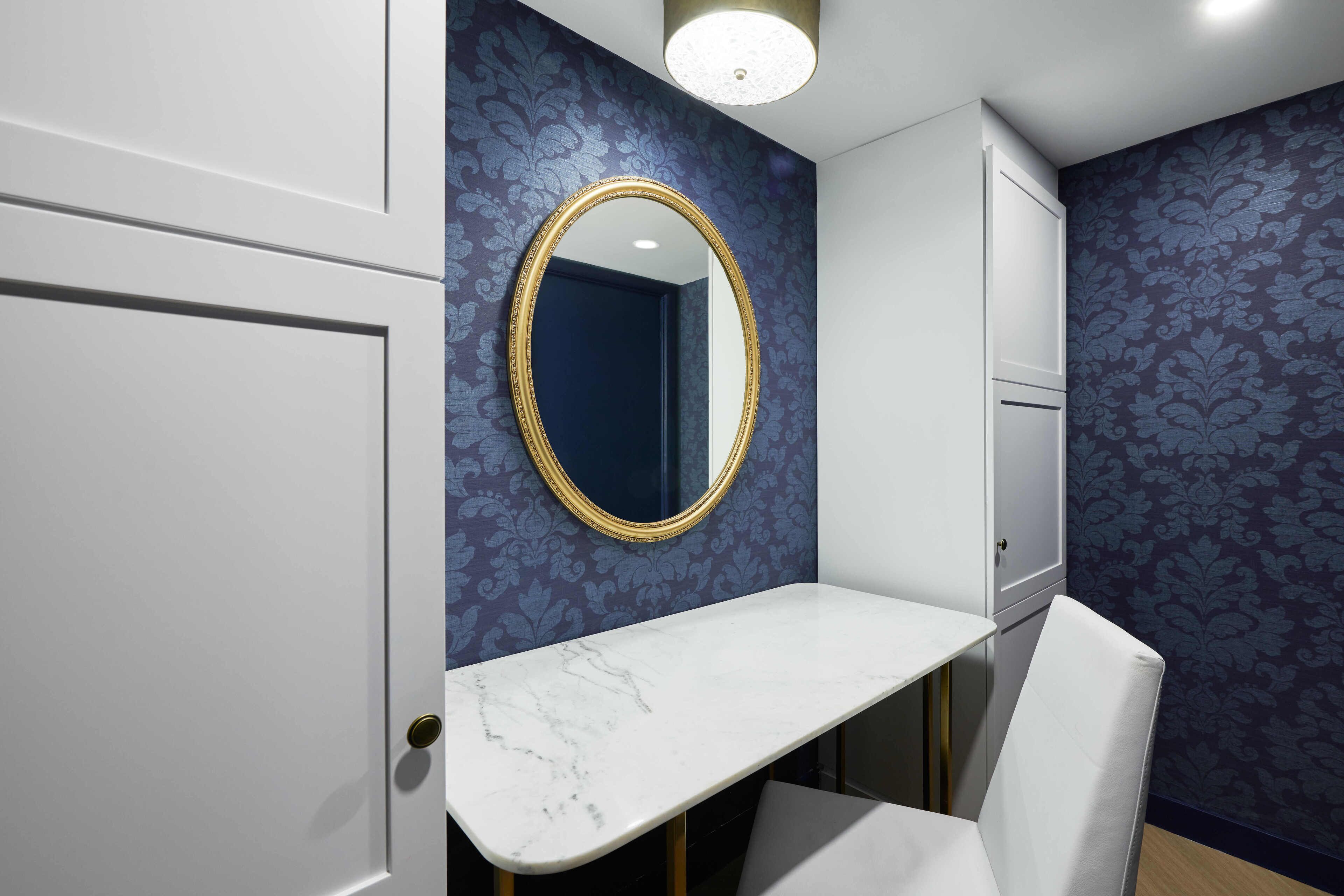 A bathroom with a white vanity, a gold-framed mirror, and blue patterned wallpaper.