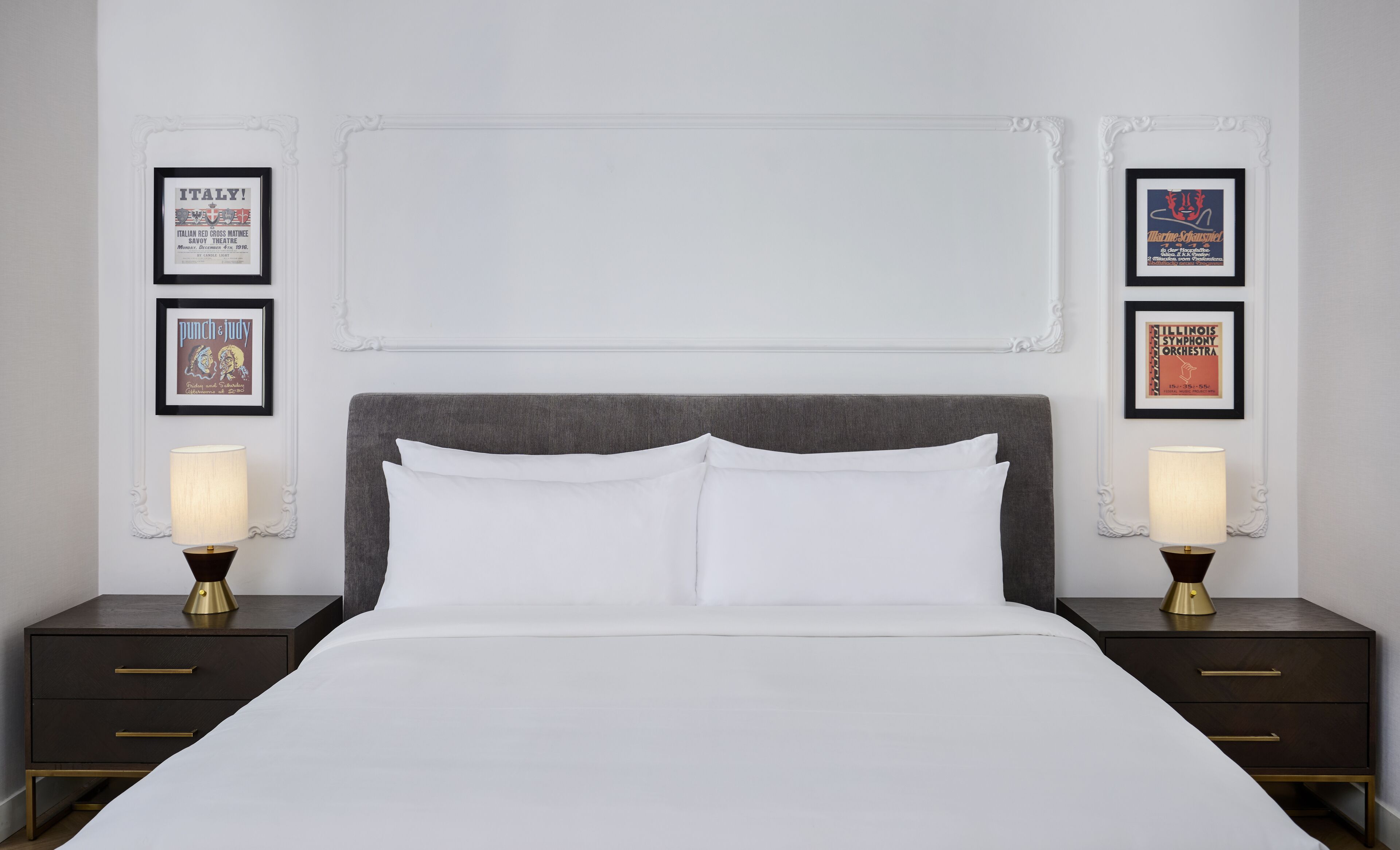 A hotel room with a large bed, two bedside tables, and framed posters on the walls.