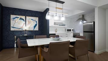 A modern kitchen with a marble countertop, stainless steel appliances, and a dining area with a white table and brown chairs.