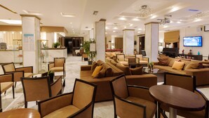 A hotel lobby with seating areas, a reception desk, and a television screen. - Venus Hotel & Suites (Zakynthos)