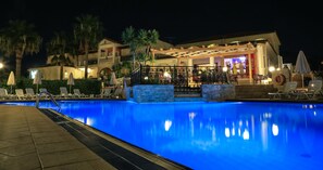 A swimming pool with lounge chairs and umbrellas, a covered seating area, and a building with a bar. - Venus Hotel & Suites (Zakynthos)