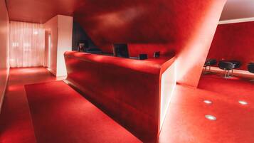 A red reception desk with a modern design, a white wall, and a red carpeted floor.