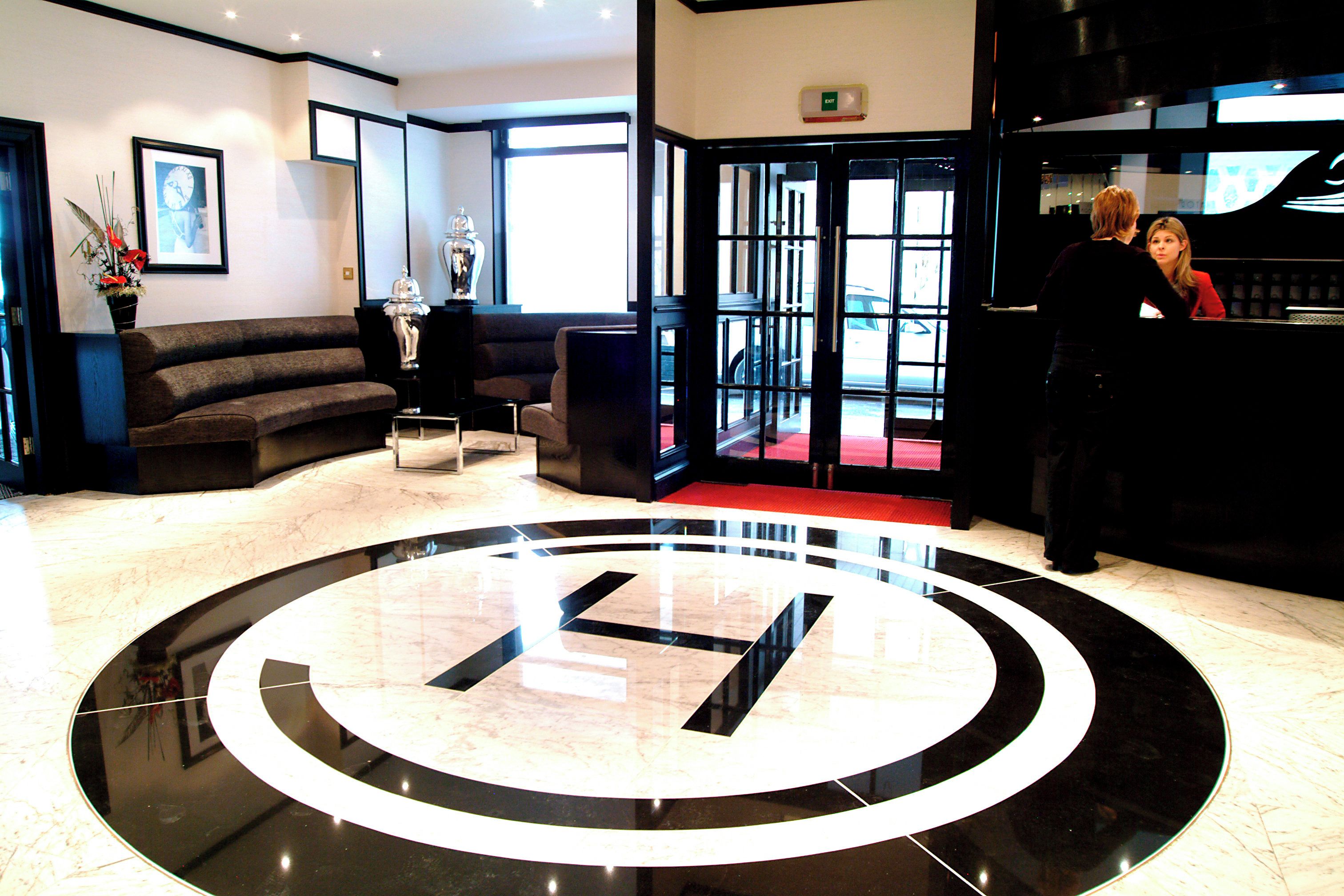 Un vestíbulo de hotel con una recepción, un área de estar con sofás y un gran emblema circular en el piso.