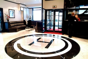 Un hall d’hôtel comprenant un comptoir d’accueil, un espace salon avec des canapés et un grand emblème circulaire au sol.