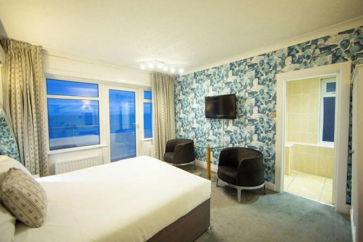 Une chambre d’hôtel avec un lit, deux chaises, une télévision et un balcon avec vue.