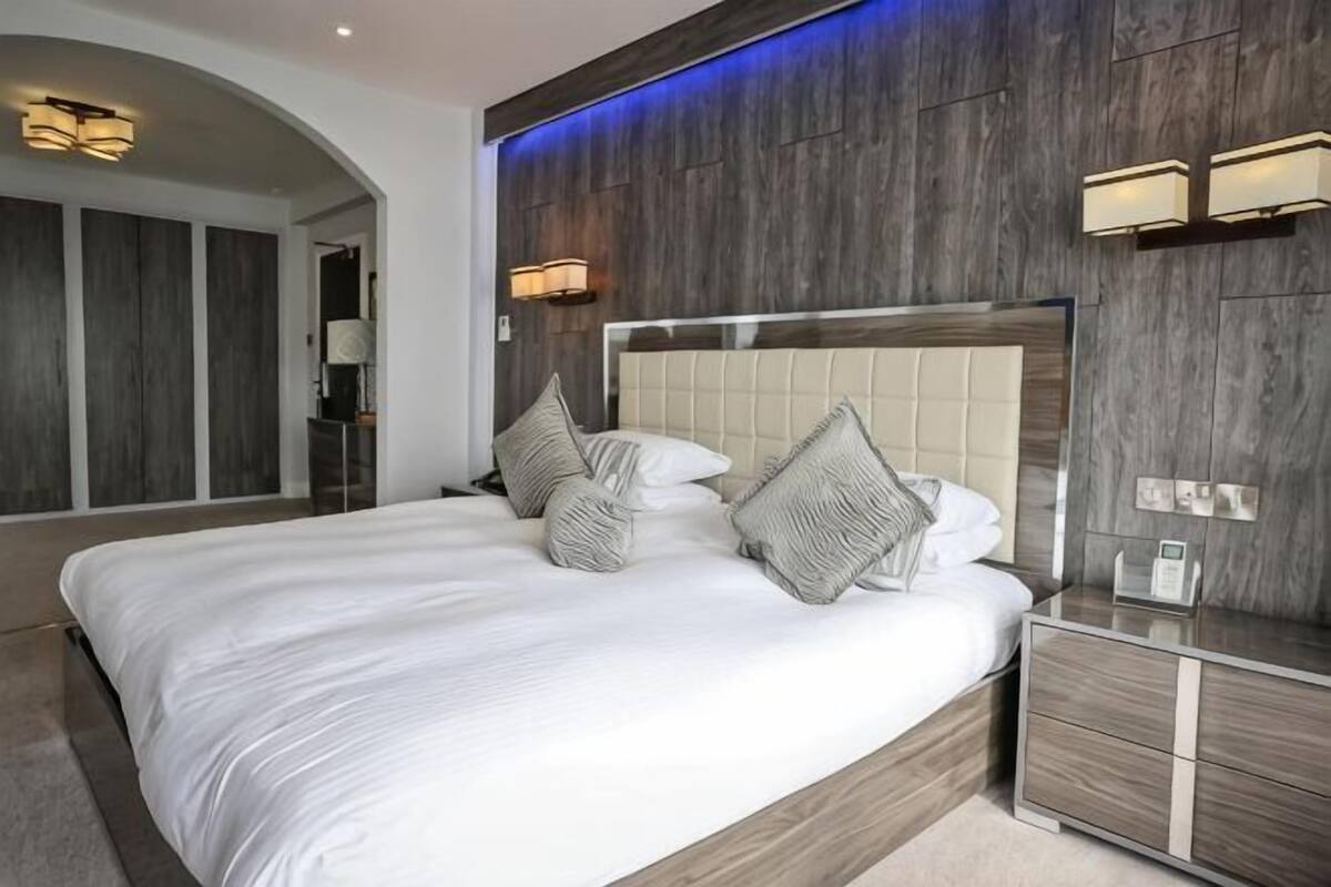 Una camera d'albergo moderna con un grande letto, una testiera in legno e illuminazione integrata.