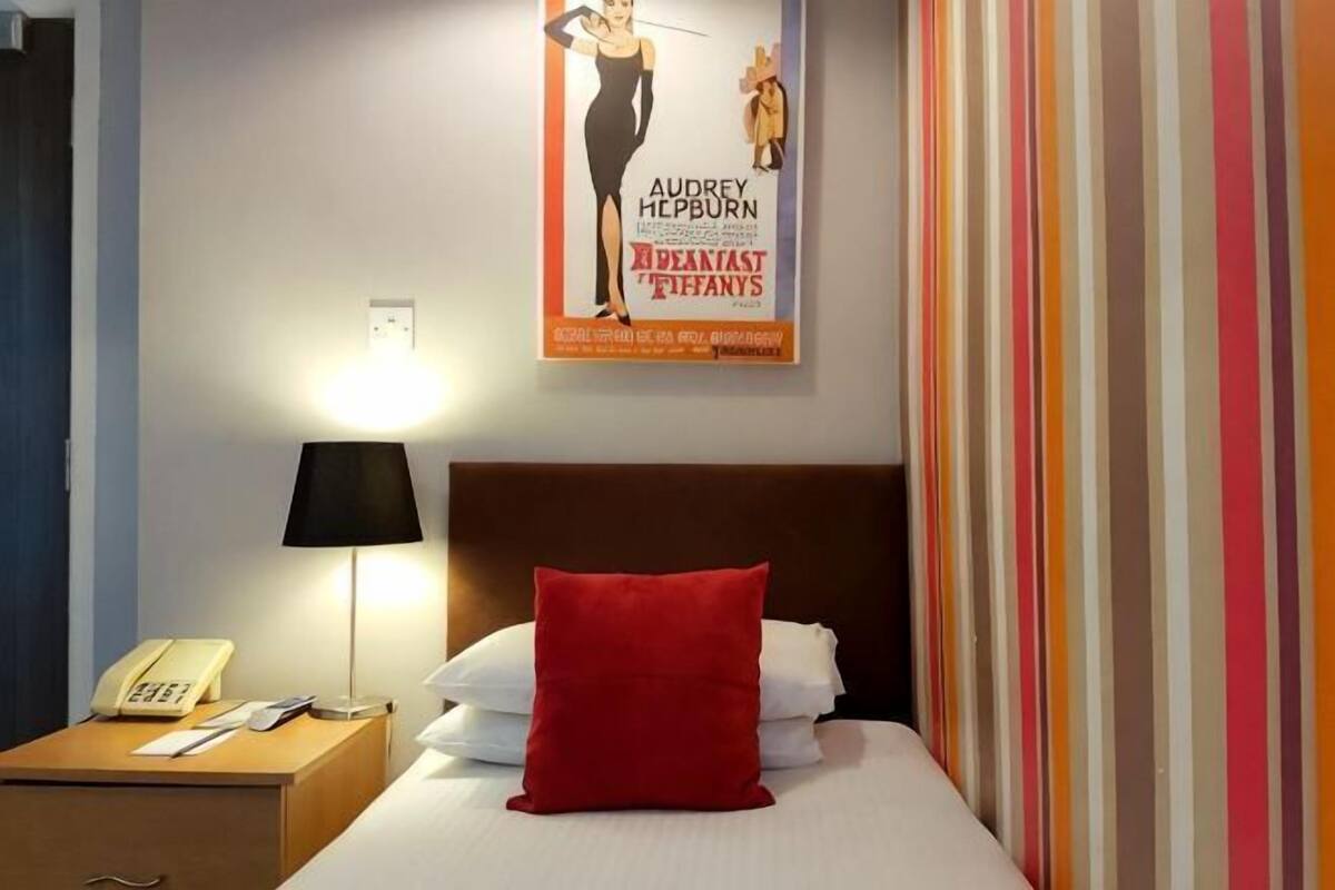 Una camera d'albergo con un letto, un comodino con una lampada, un telefono e un quadro appeso al muro.