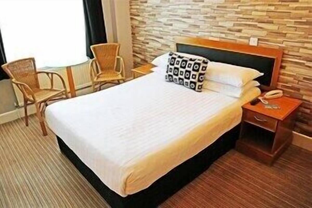 Una camera d'albergo con un letto, un comodino, una sedia e una parete con decorazione in pietra.