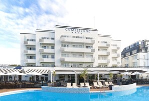 Ein mehrstöckiges Hotel mit Poolbereich, Außenbereich zum Sitzen und einer Bar.