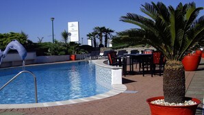 Een zwembad met een badmeesterstand, ligbedden en een bord voor 'The Cumberland Hotel Bar & Dining'.