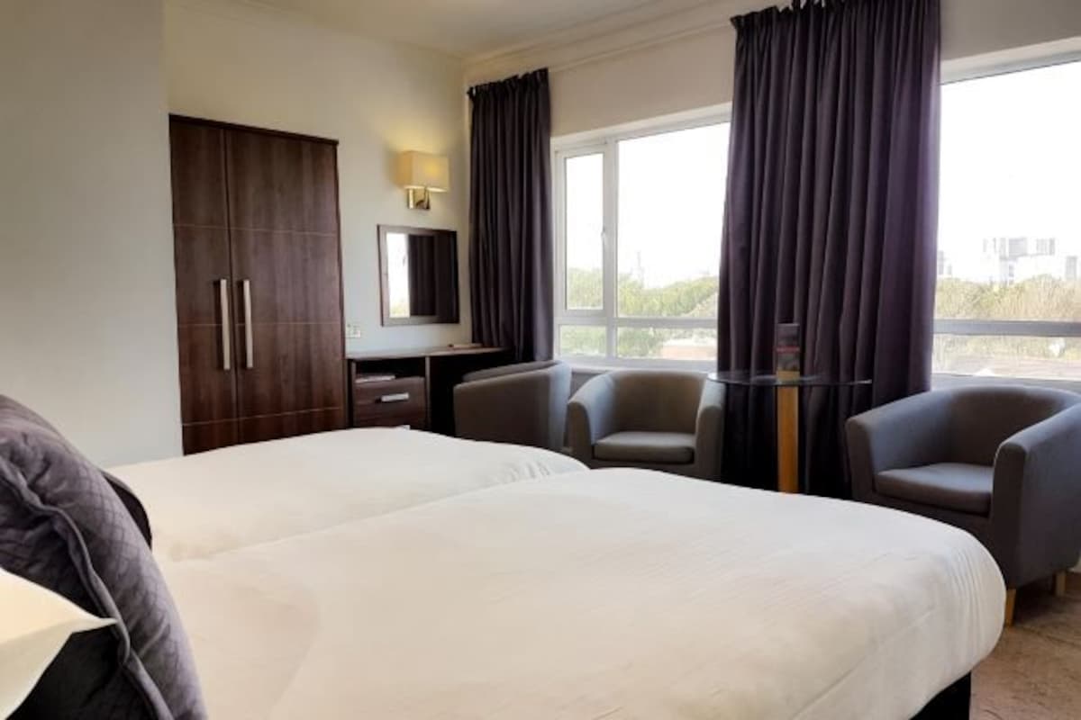 Una habitación de hotel con cama, dos sillones, un escritorio, televisión y ventana con cortinas.
