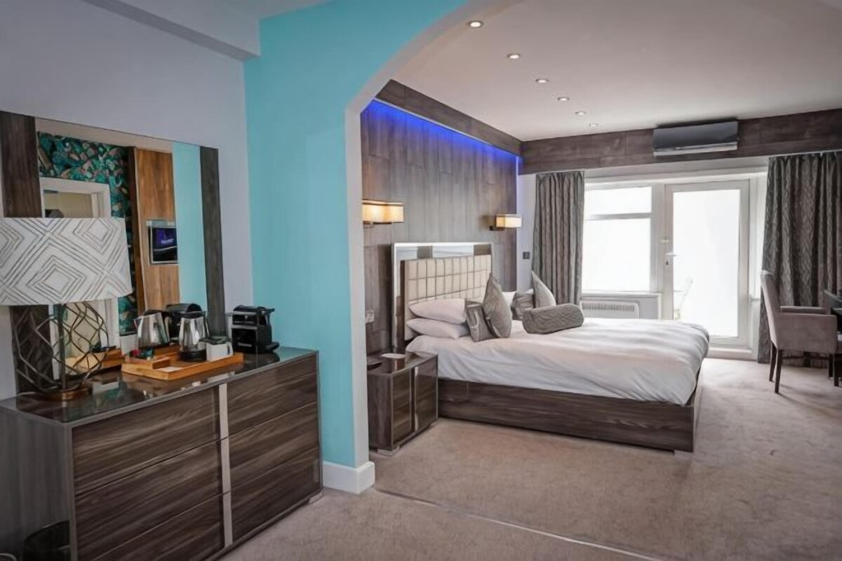Ein modernes Hotelzimmer mit Bett, Nachttisch, Lampe und Blick ins Freie.