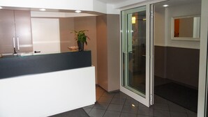 Cocina moderna con encimera blanca, puerta de cristal que da al baño y una planta en maceta sobre la encimera.