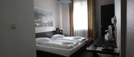 A hotel room with a bed, a desk with a telephone, and a lamp.