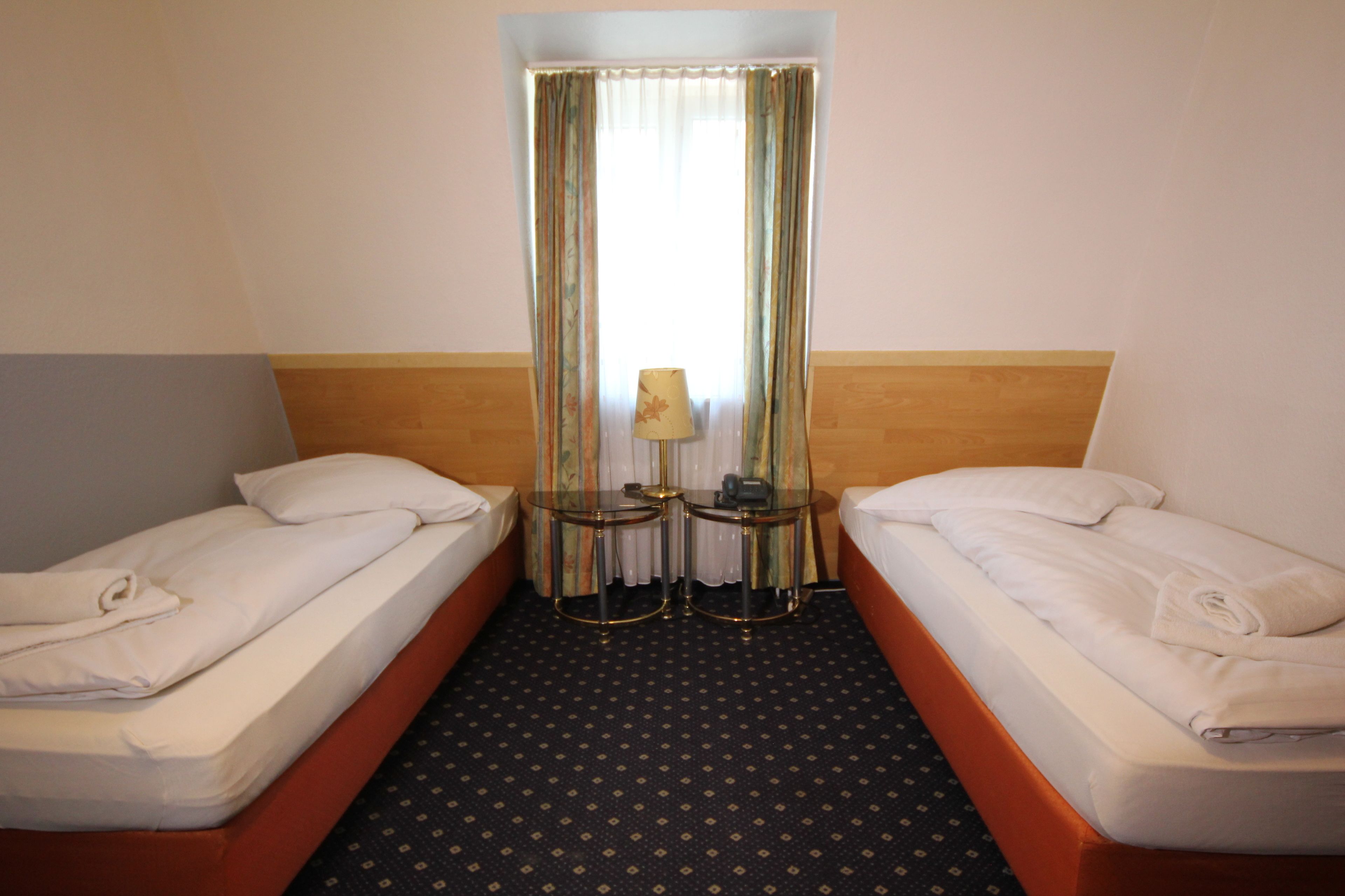 Una habitación de hotel con dos camas individuales, una mesita con una lámpara y una ventana con cortinas.