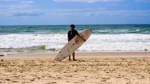 A person holding a surfboard on a beach with waves in the background.