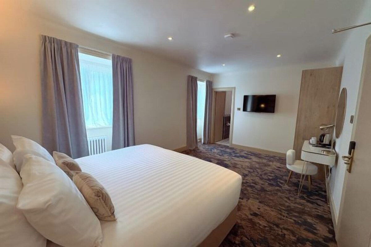A hotel room with a large bed, a television, a desk with a chair, and a bathroom with a mirror.