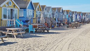 A row of beach huts with wooden benches and tables, a clear sky, and a sandy beach.