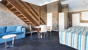 A modern room with a brick wall, a wooden staircase, a blue sofa, a small table, and a bed with striped bedding. - Marion Motel and Apartments (Plympton Park)