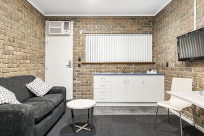 Eine kleine Küche mit Backsteinwand, weißen Schränken, Spüle und einem Flachbildfernseher.