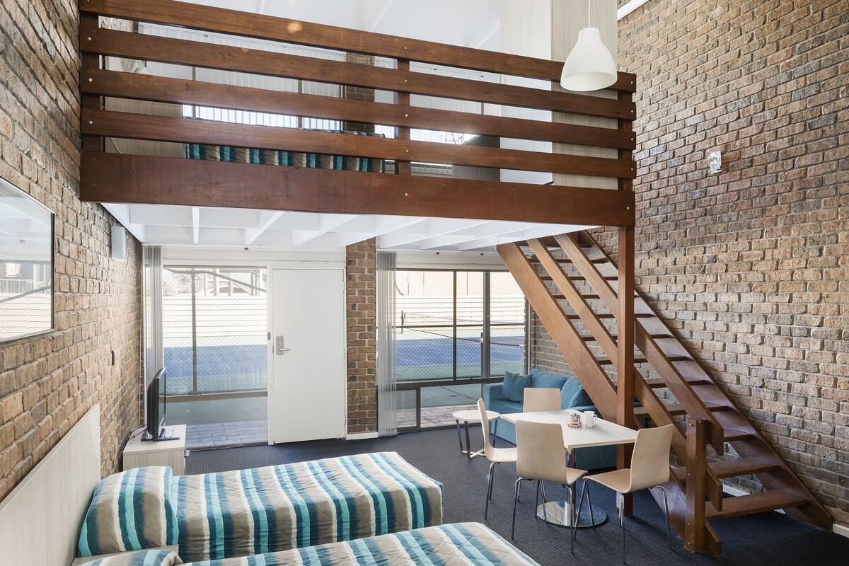 A modern room with a loft area, a staircase, and a seating area with a table and chairs.