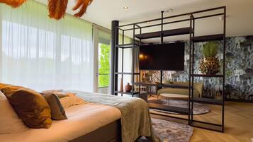 Un dormitorio moderno con una cama grande, televisor y zona de estar con vistas a zonas verdes.