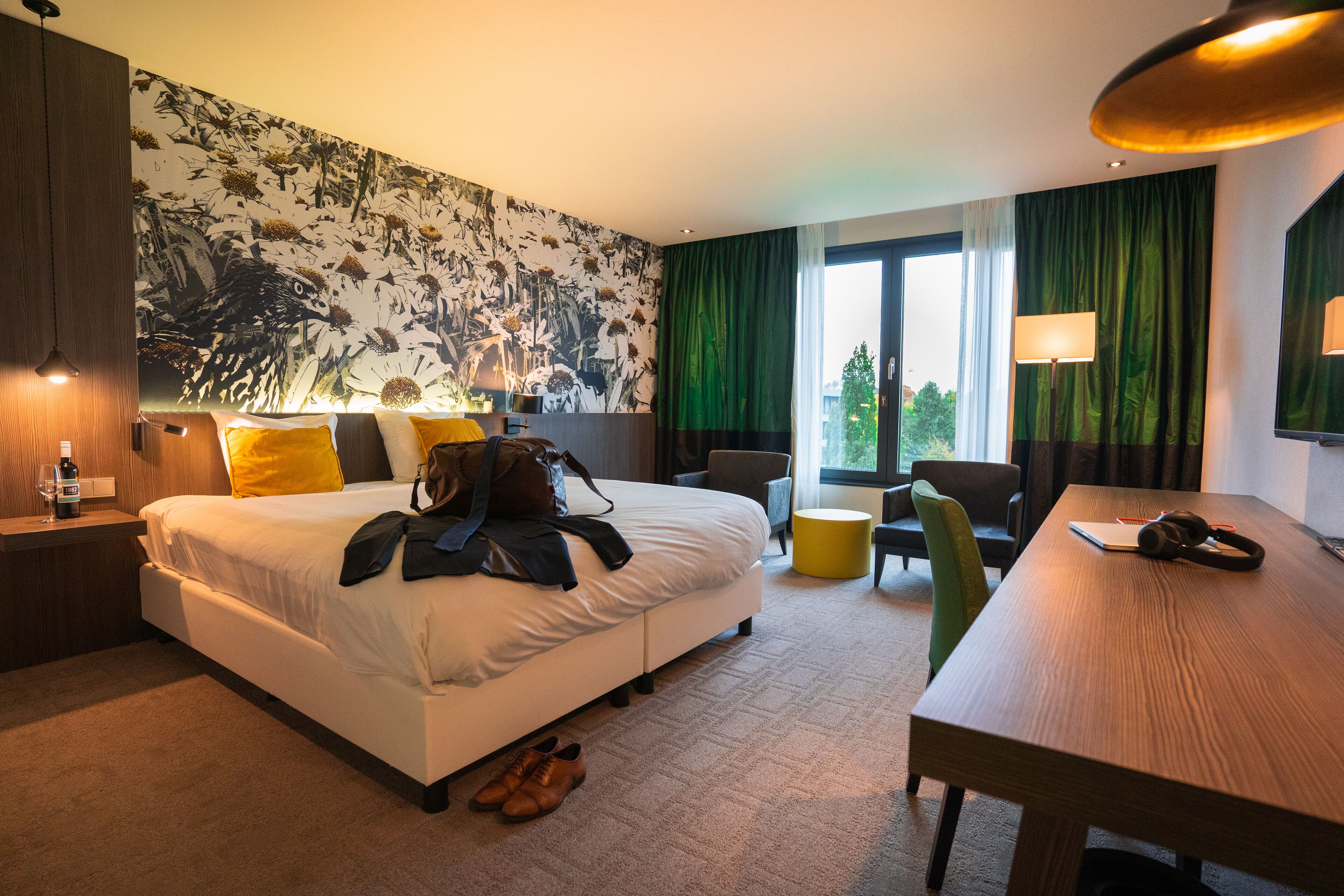 Een hotelkamer met een groot bed, een bureau, een stoel, een lamp en uitzicht op de omgeving.