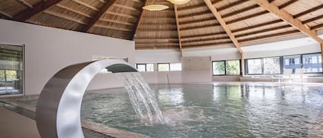 A modern indoor swimming pool with a wooden ceiling and a large, curved water feature.