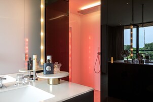 A modern bathroom with a white vanity, a round mirror, and a red accent wall.