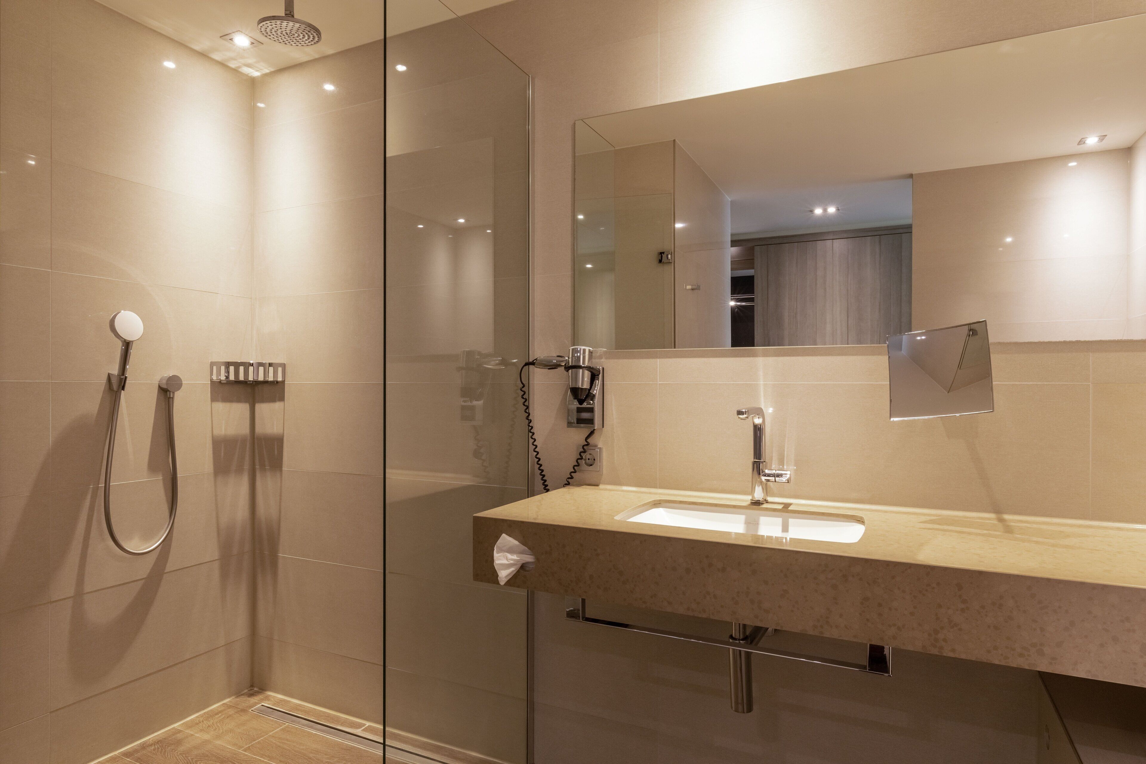 Une salle de bain moderne avec une douche à l’italienne en verre, un lavabo avec un miroir et un porte-serviettes.