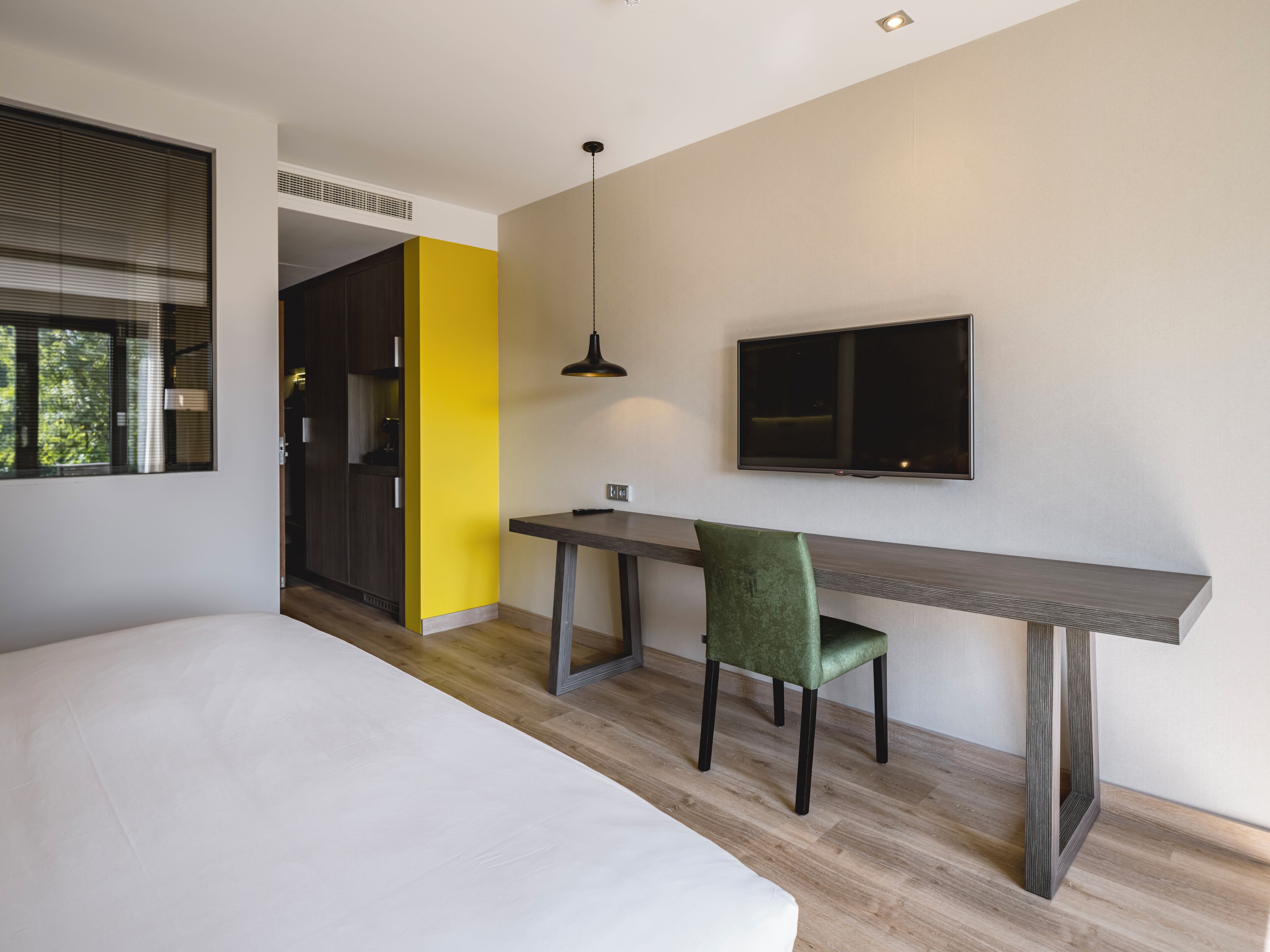 Een moderne slaapkamer met een groot bed, een bureau met stoel, een televisie en een raam met jaloezieën.