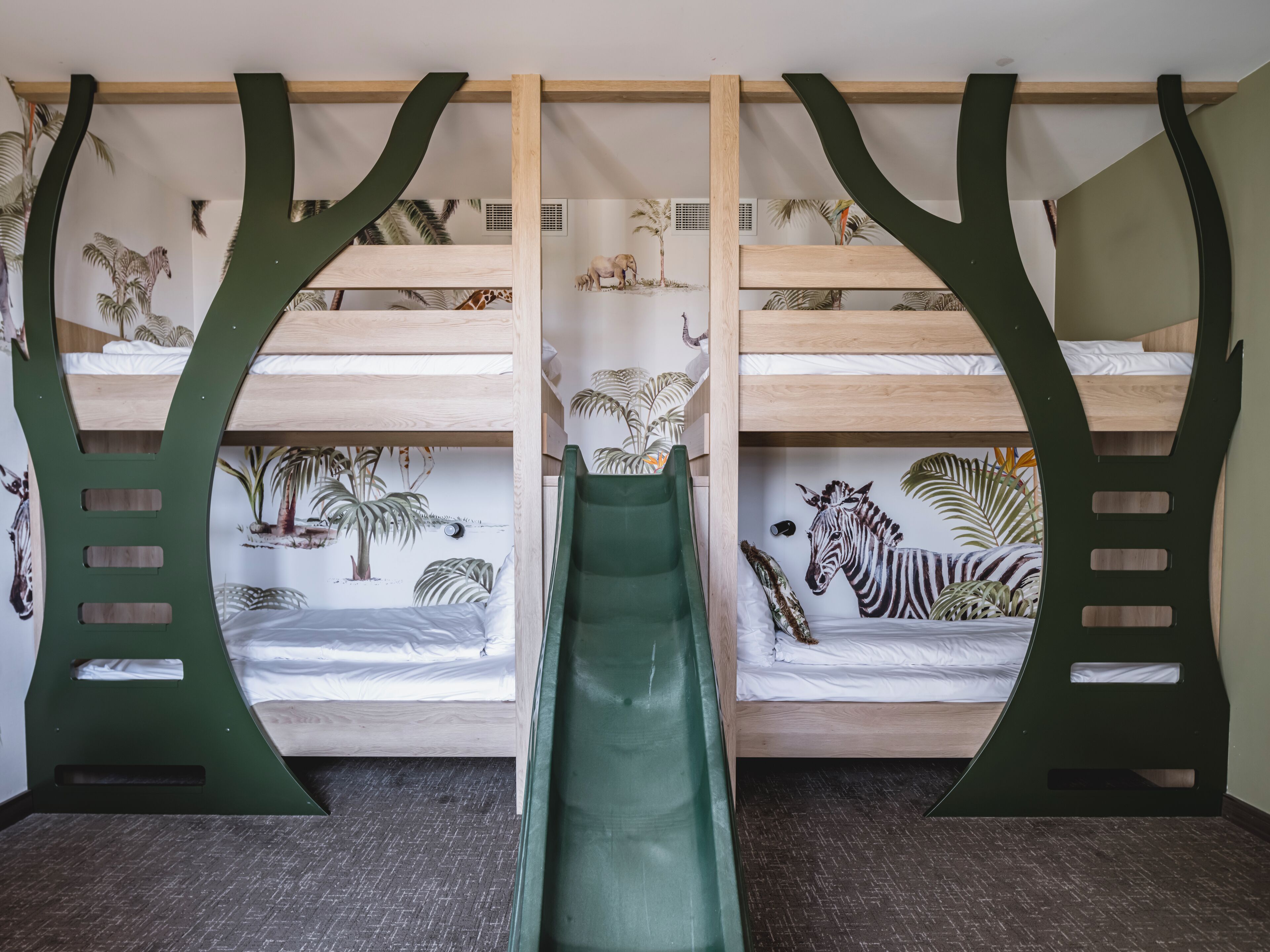 Un lit superposé avec un toboggan, entouré de peintures murales représentant des animaux et des plantes.
