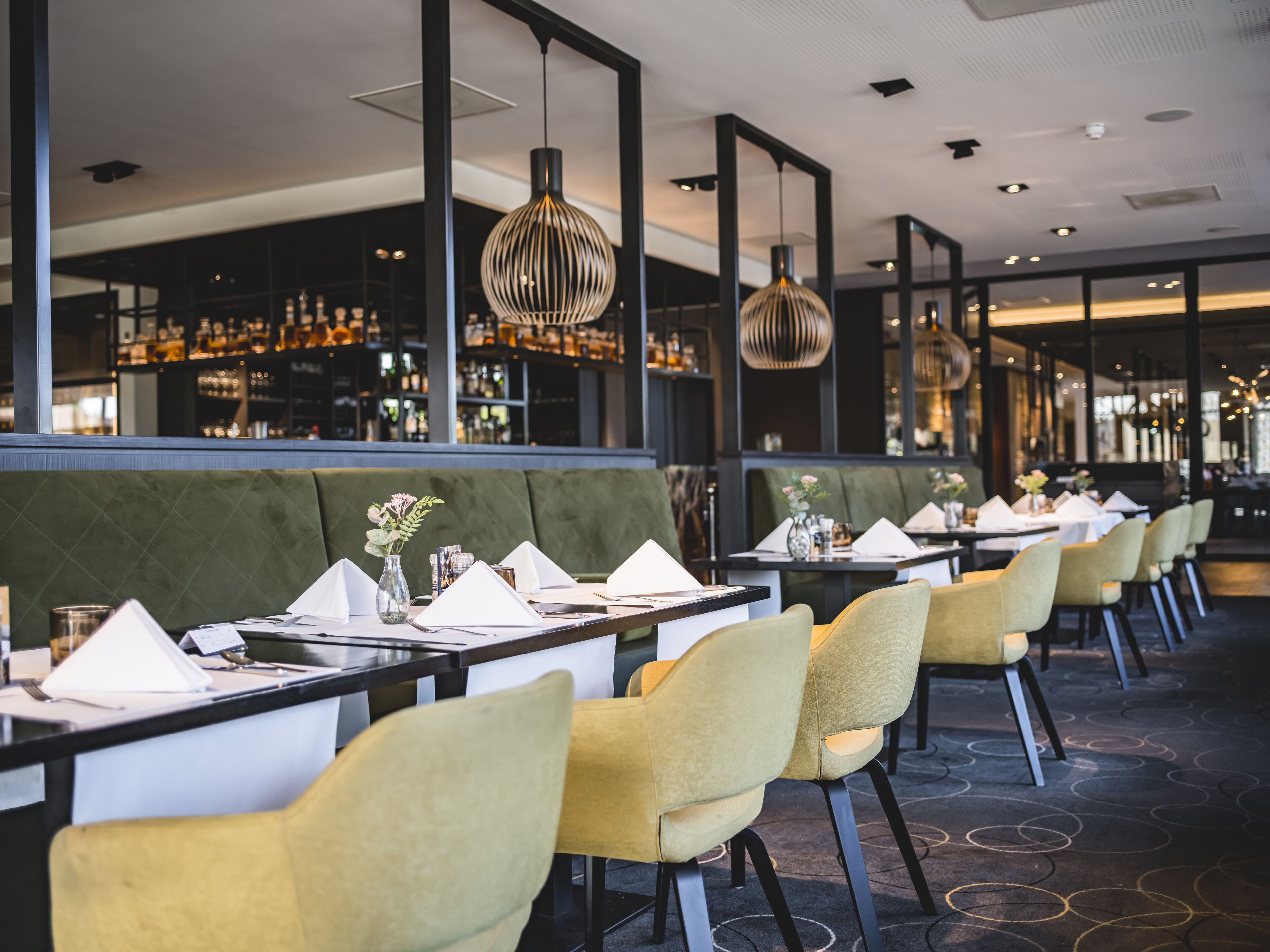 Un restaurante con una barra larga, asientos tapizados en verde y sillas amarillas.