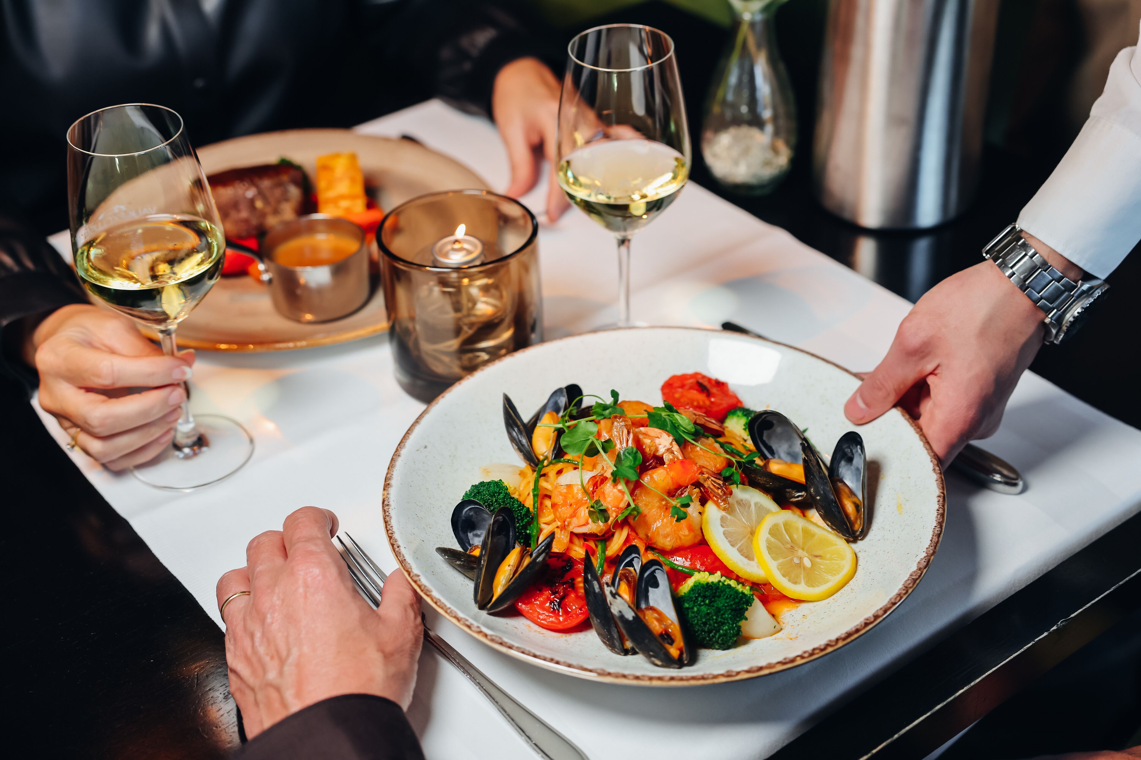 Une table à manger avec un plat de fruits de mer, des verres à vin et une bougie.