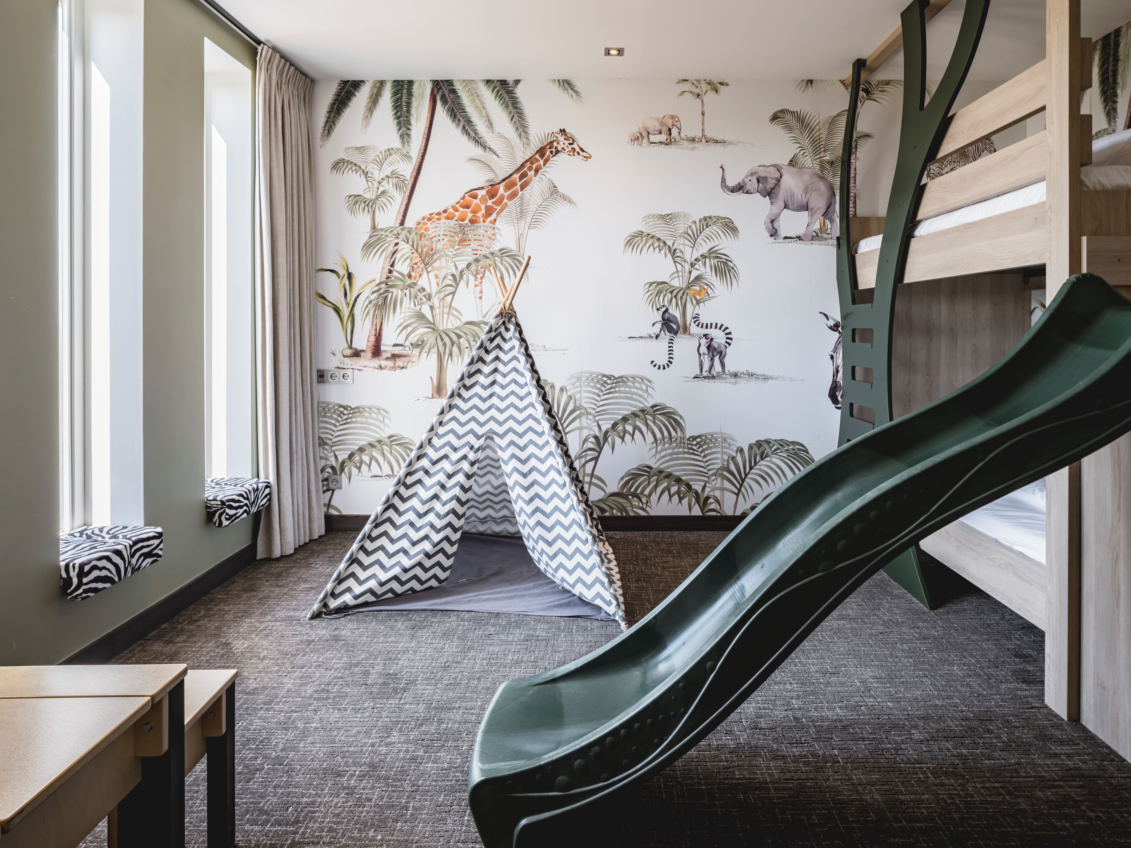 Una habitación con un tobogán, una cama con estampado de cebra, una tienda de campaña y un mural de animales.