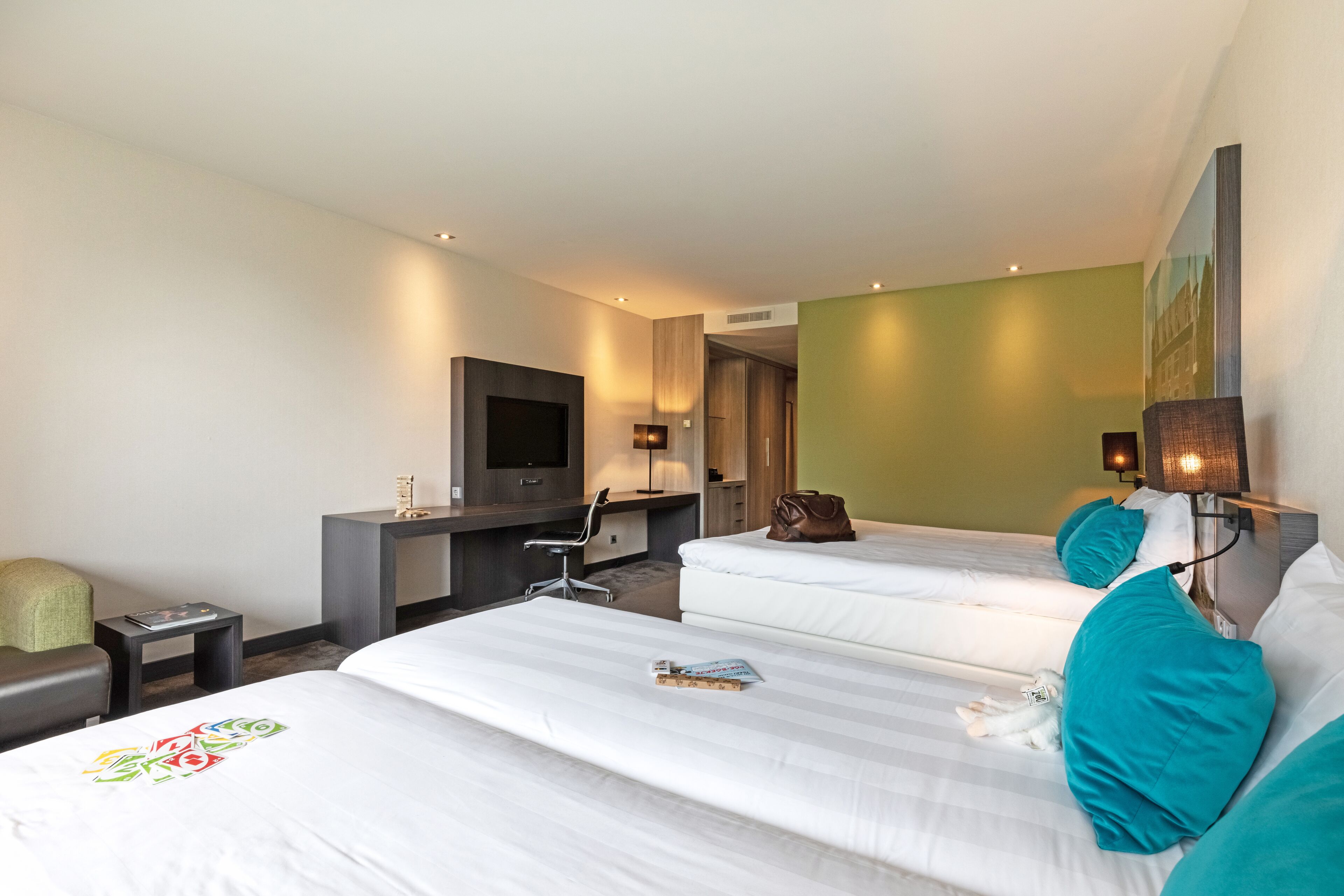 Hotelkamer met twee bedden, een bureau, een stoel, een televisie en een klein tafeltje met een tijdschrift.