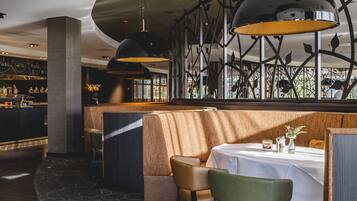 Interior de un restaurante con techo curvo, iluminación colgante moderna, zona de bar y mesa preparada para comer.