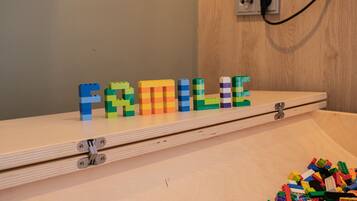 Een houten plank waarop LEGO letters het woord “FAMILY” spellen, en een stapel LEGO stukjes op de vloer.