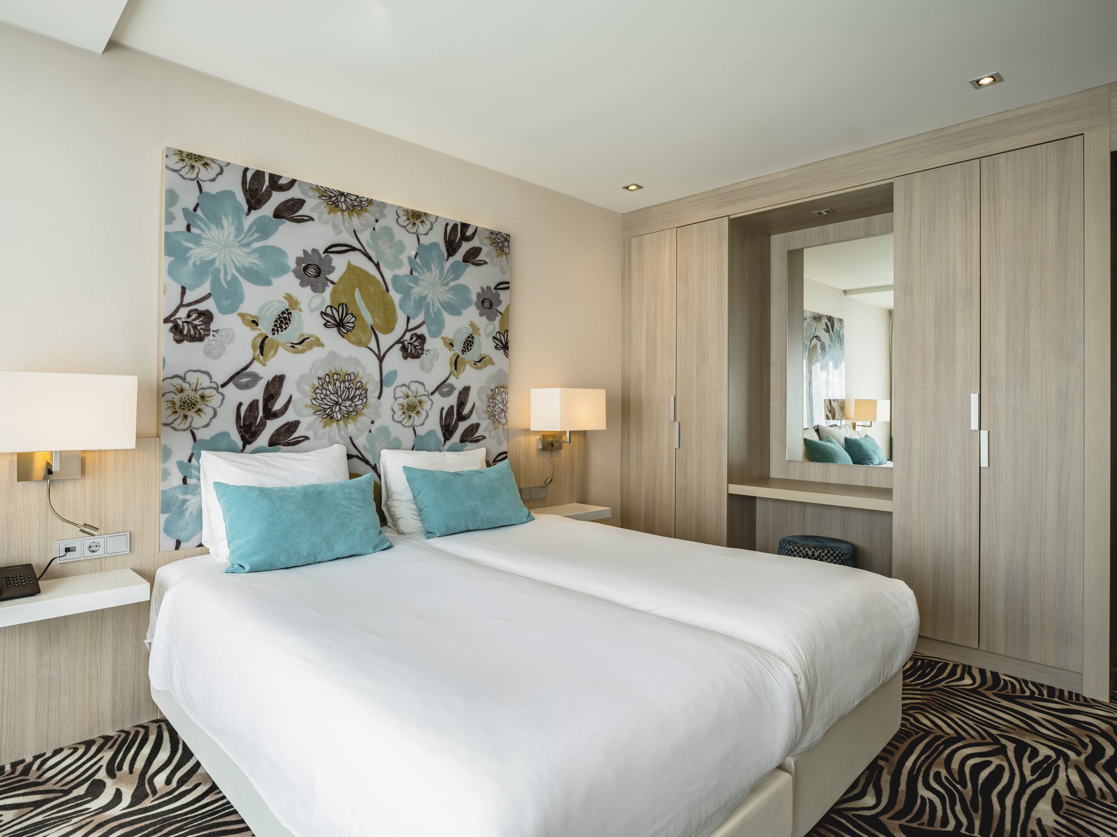 Een hotelkamer met een groot bed, twee bedlampen, een spiegel en een kledingkast.