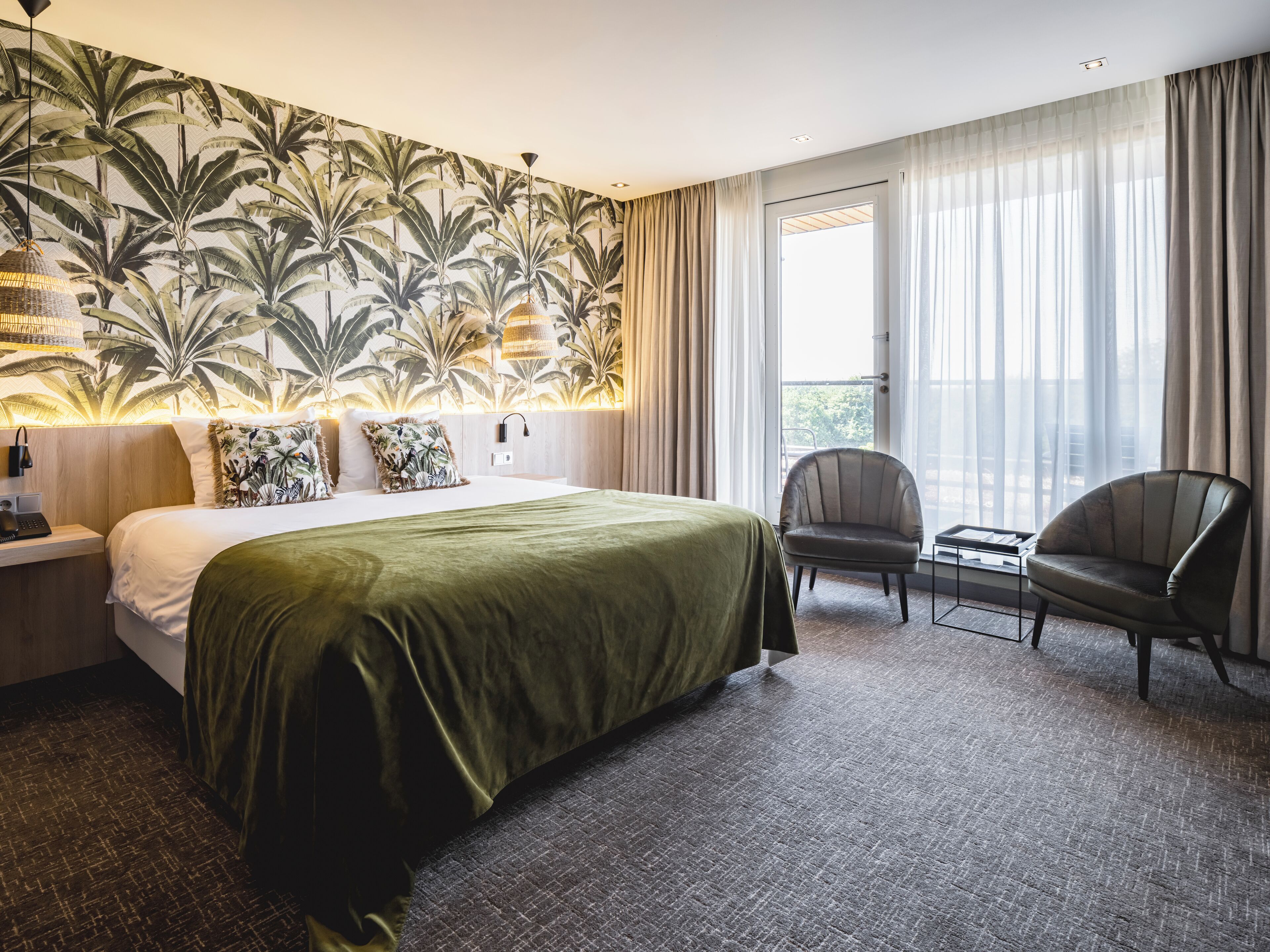 Quarto de hotel com uma cama grande, uma cadeira, uma mesa pequena e vista para o exterior.