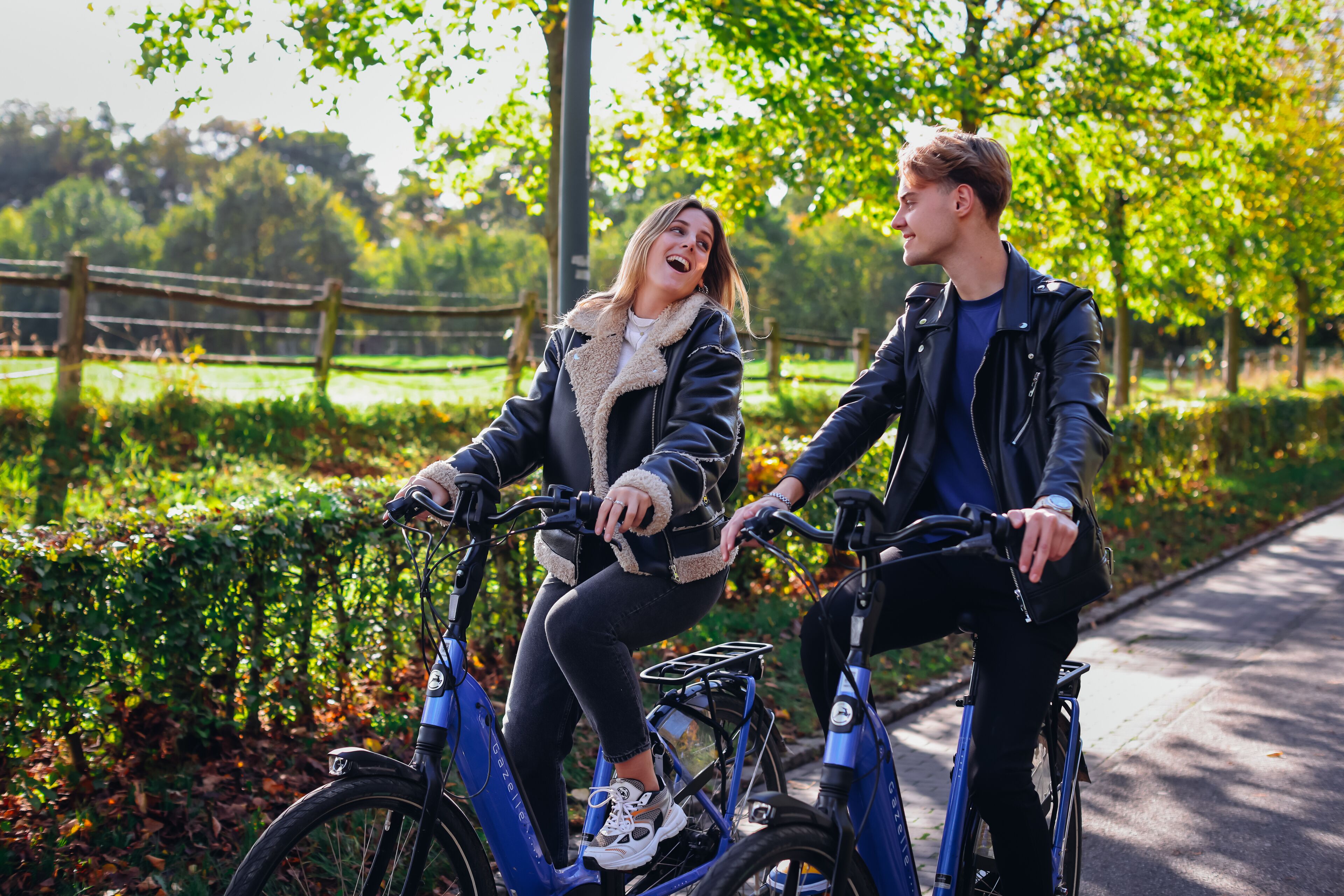 Two people on a tandem bicycle in a park with greenery and a fence in the background.