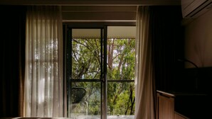 Un dormitorio con una cama, un aparador de madera y un ventanal corredizo que da a un balcón con árboles.