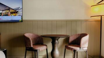 A room with two upholstered chairs, a round table, a television mounted on the wall, and a floor lamp.