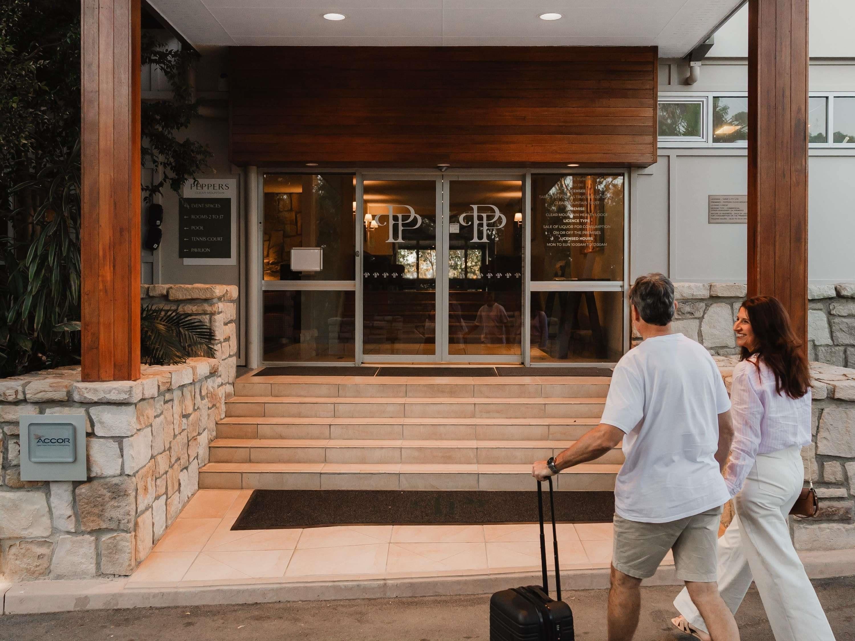 Fachada de hotel de piedra, con columnas de madera y un cartel claro.