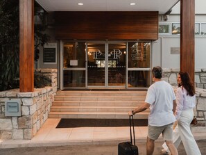 Fachada de hotel de piedra, con columnas de madera y un cartel claro.