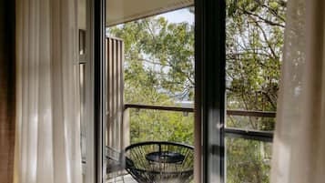 A balcony with a chair and a table, overlooking a tree-filled area.